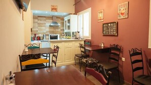 A dining area with a wooden table and chairs, a kitchen in the background, and a red wall with posters. - Acronafplia Pension B&D (Nafplio)