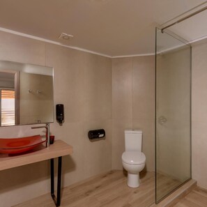 A bathroom with a glass shower enclosure, a white toilet, a red sink, and a mirror. - Katrin Suites (Hersonissos)