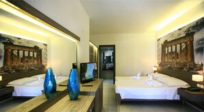 A hotel room with two beds, a TV, a desk, and artwork depicting ancient ruins. - Katrin Suites (Hersonissos)