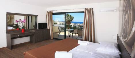 A hotel room with a bed, a desk, a TV, a balcony with a view of the sea, and a large mirror.