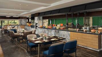 Un restaurante moderno con pisos de mármol, sillas tapizadas en azul y una zona de cocina con un revestimiento verde tipo espiga.