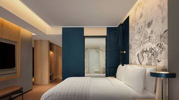 A modern hotel room with a large bed, a bedside table with a lamp, a wardrobe, and a bathroom visible through an open door.