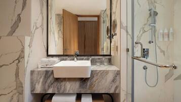 Un baño con lavamanos de mármol, espejo, ducha y toallero.