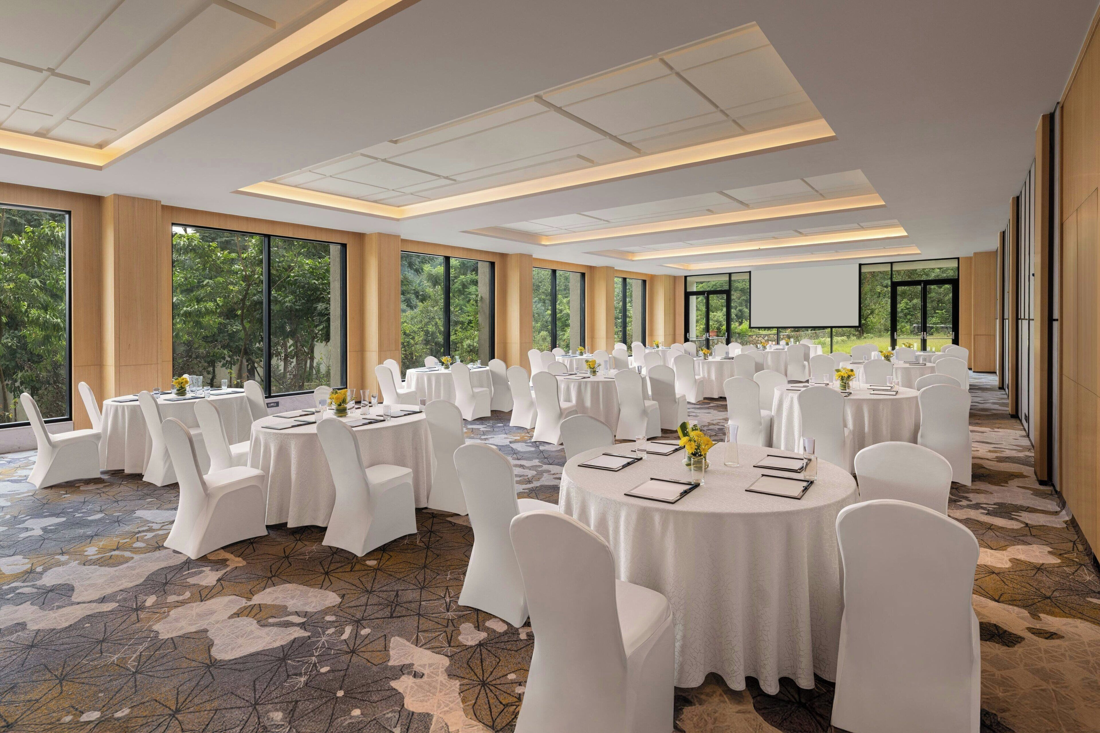 A conference room with round tables, white chairs, and a large screen.