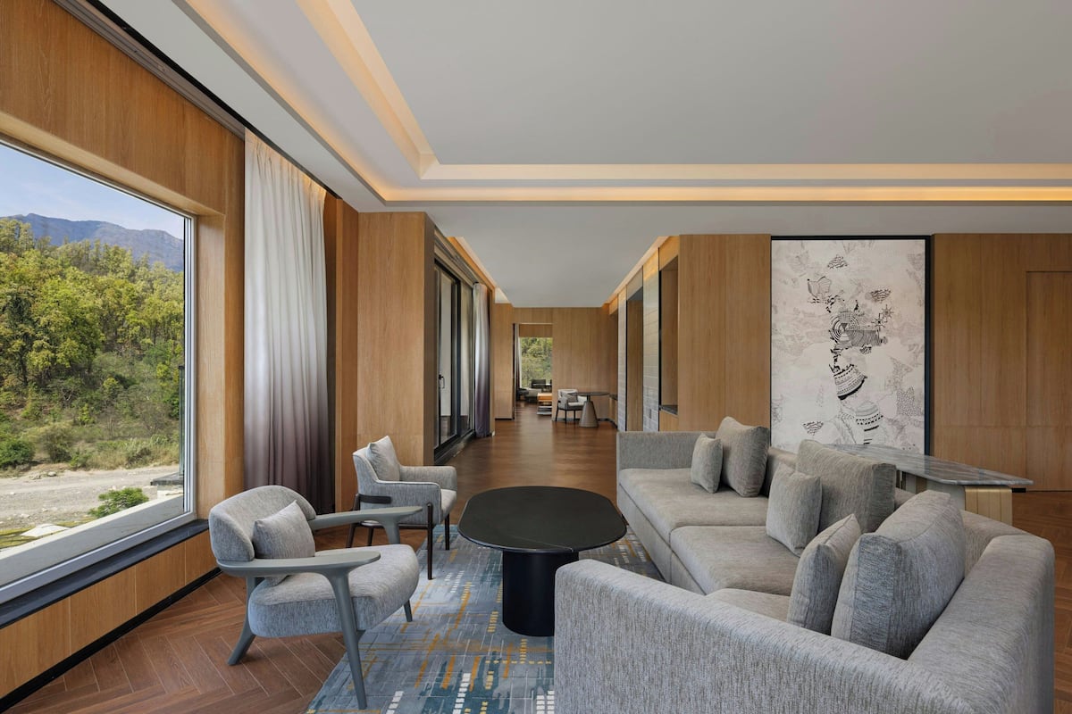 A modern interior with a sofa, chairs, a coffee table, and a large window offering a view of greenery and mountains.
