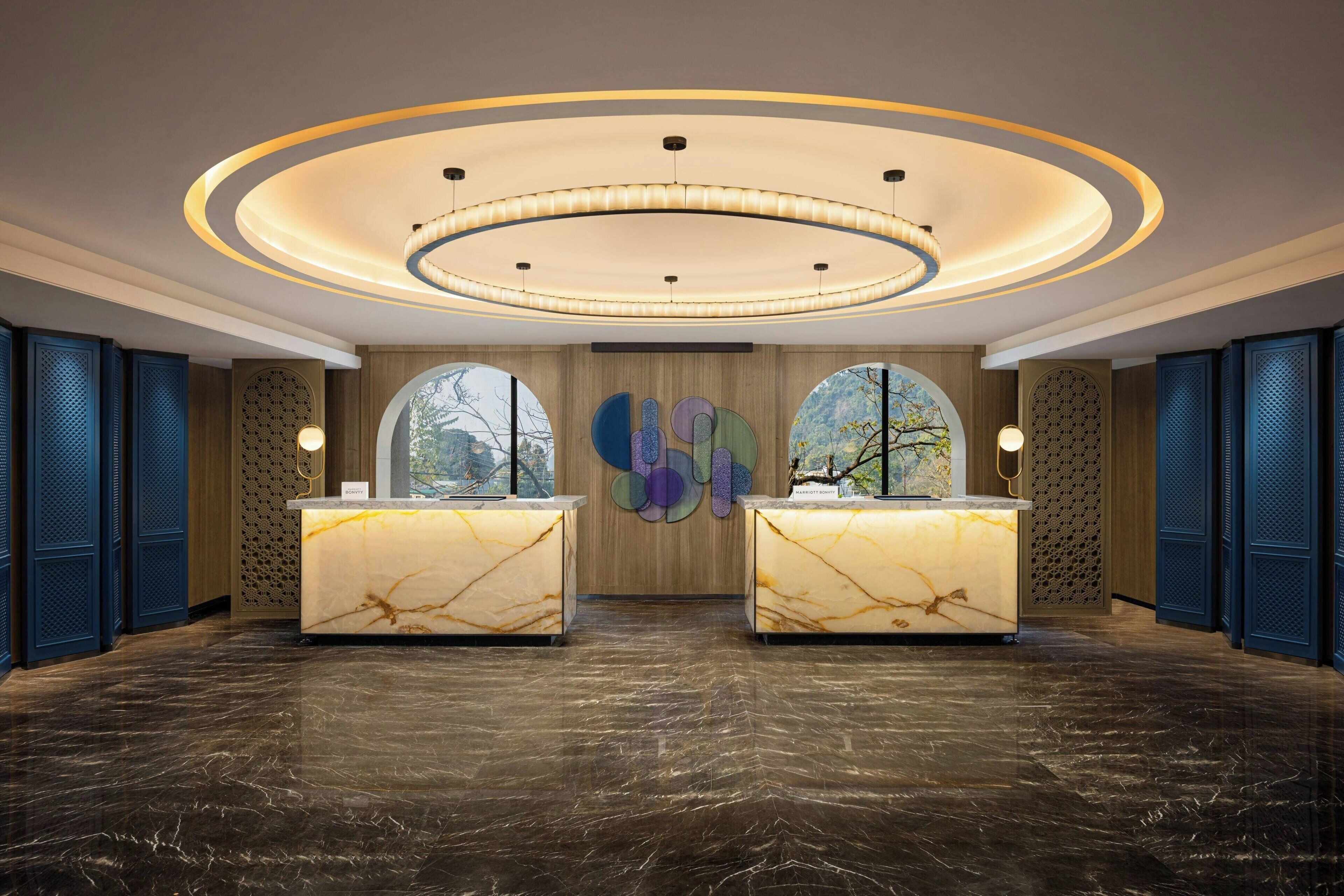 A reception area with two marble reception desks, a circular ceiling light fixture, and a large abstract wall art piece.