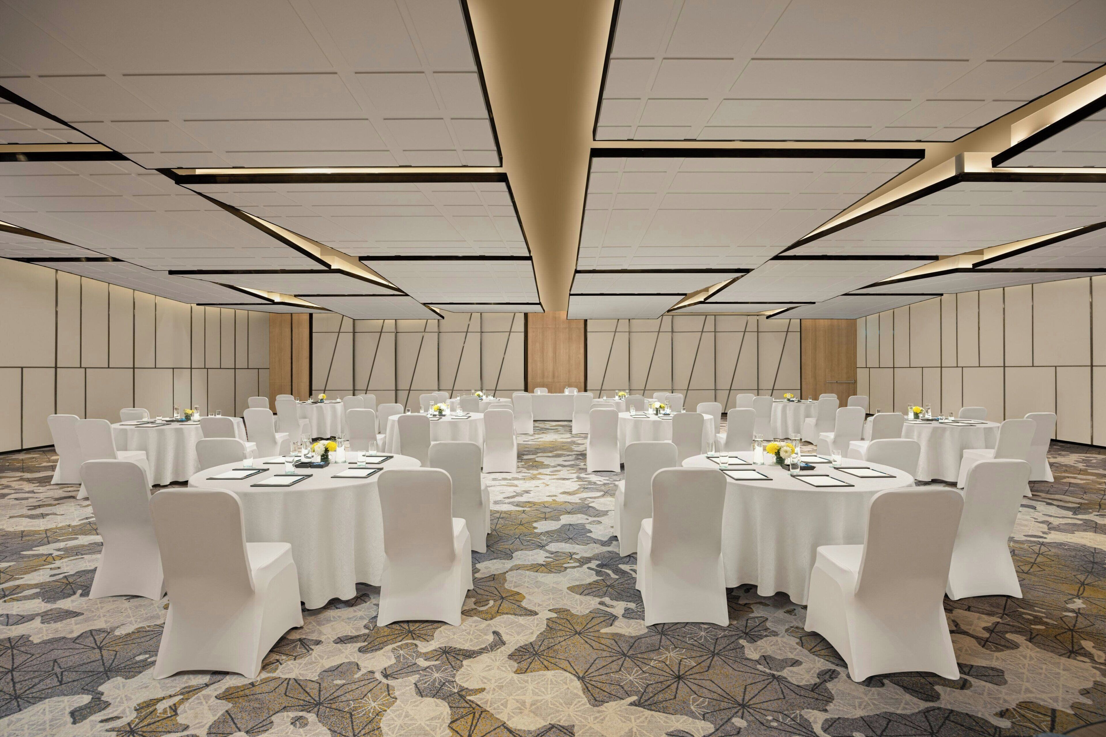 A conference room with round tables, white chairs, and a patterned carpet.