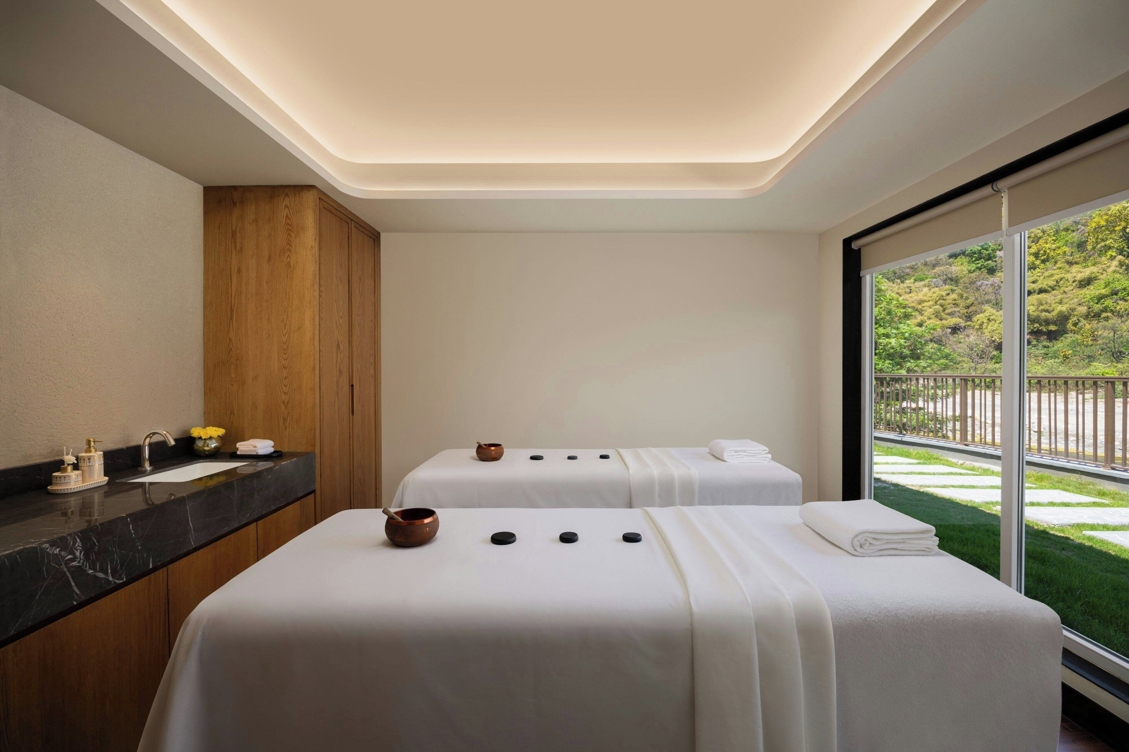 Quarto de hotel moderno com cama de spa, um armário de madeira, uma pia e uma janela grande com vista para o verde.