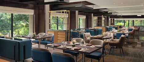 A modern restaurant with high ceilings, large windows, and a mix of seating arrangements including booths and tables.