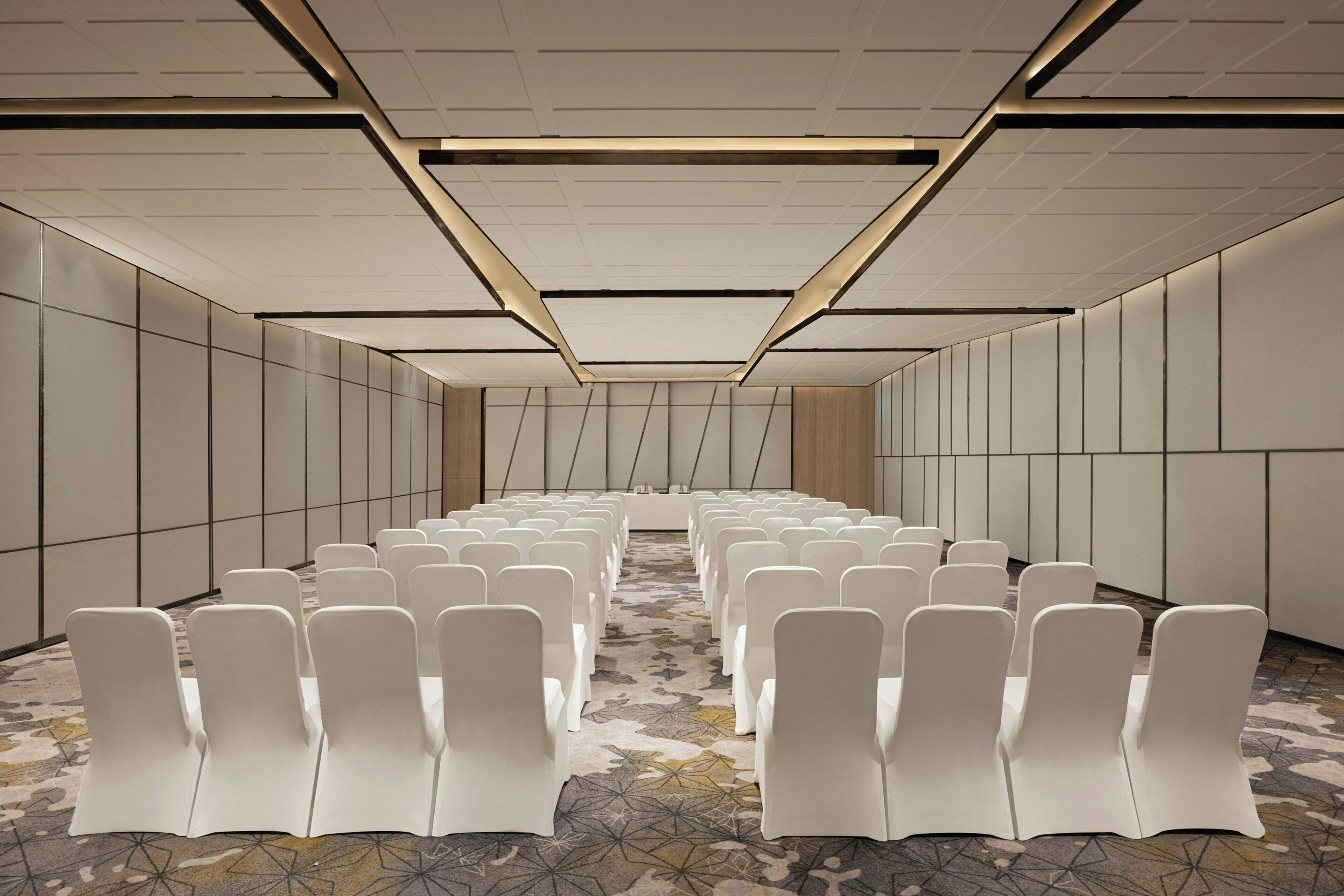 Une salle de conférence avec des rangées de chaises blanches et un tapis à motifs.