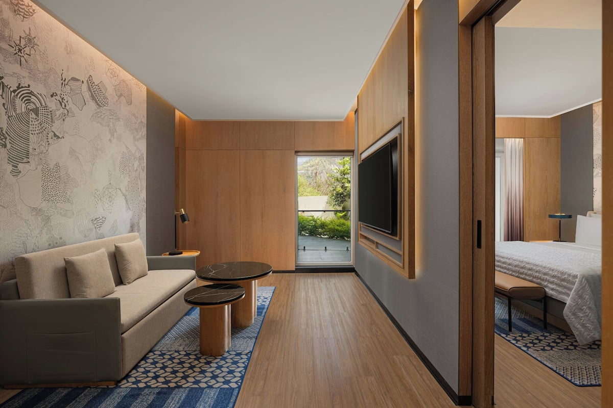 A modern hotel room with a sofa, a TV, a bed, and a small table.