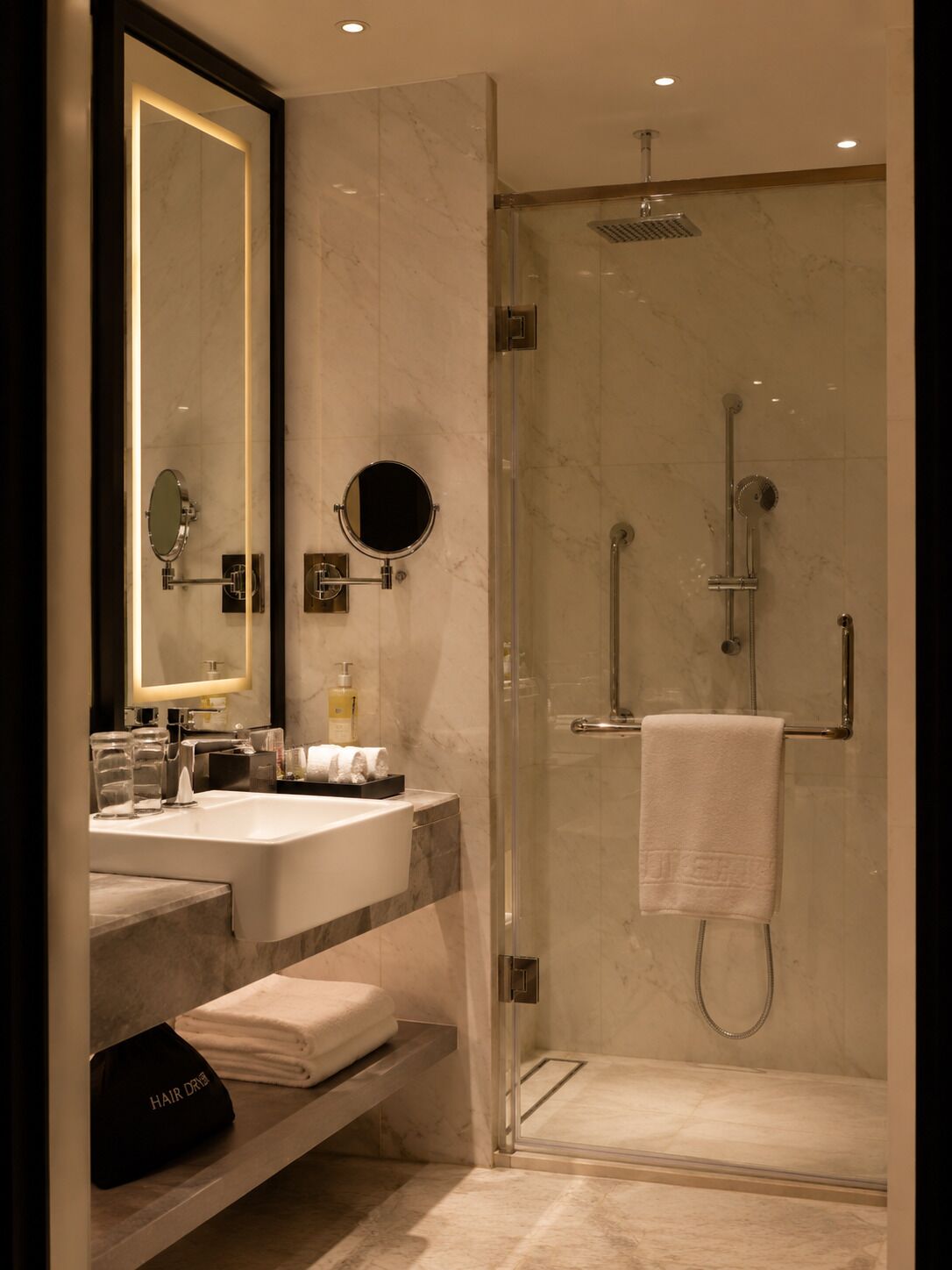 A modern bathroom with a glass-enclosed shower, a large mirror, and a vanity with a sink and towel rack.