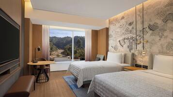 Habitación de hotel con dos camas, un escritorio, un banco, un televisor y un ventanal con vistas a un bosque.