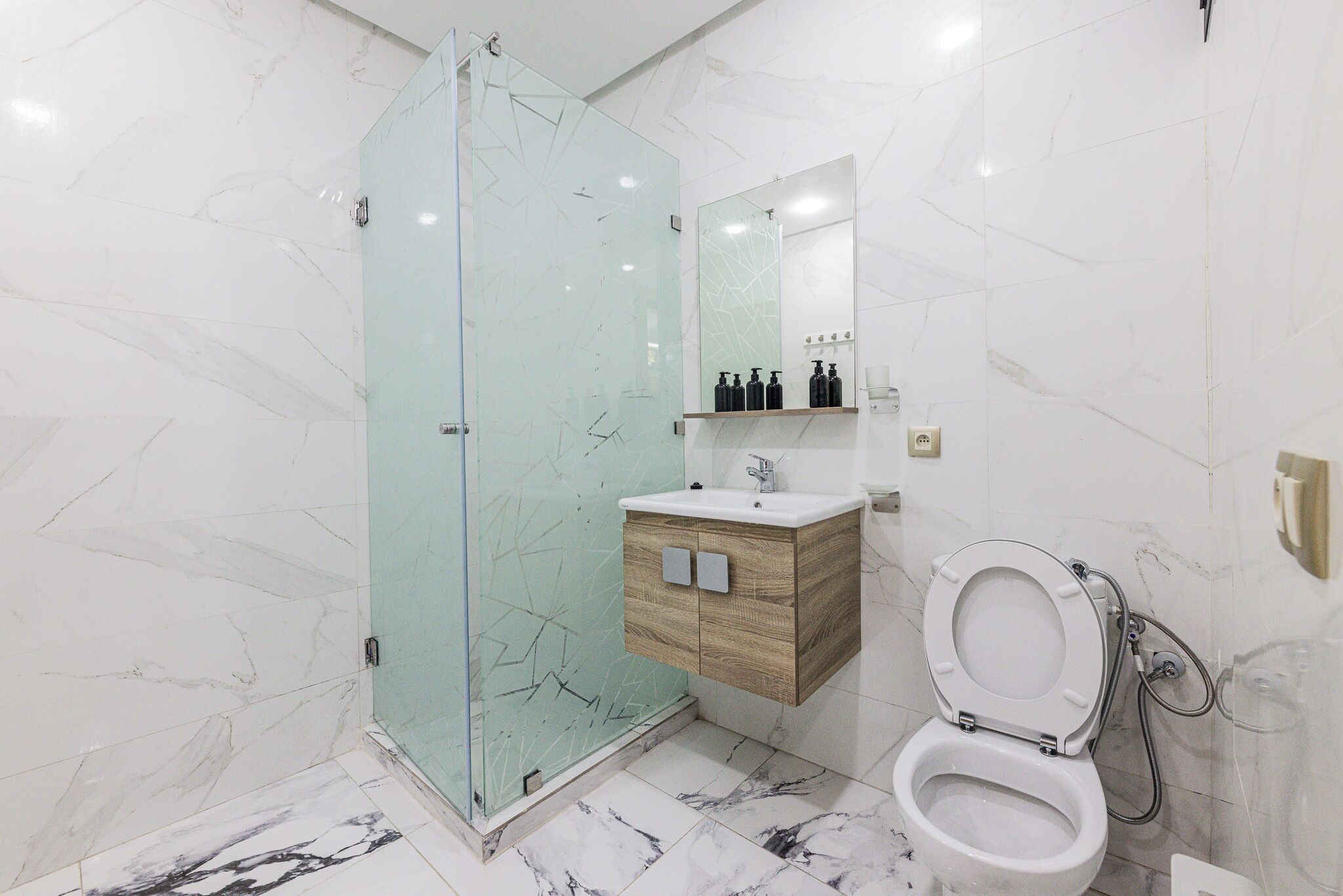 A modern bathroom with a glass shower enclosure, a wooden vanity, a white sink, and a toilet.