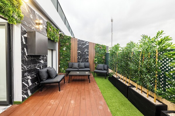 A modern outdoor patio with a wooden deck, black and white marble wall, and a green lawn area.