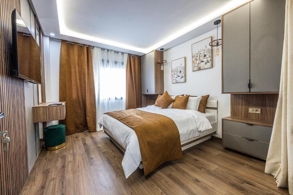 Une chambre d’hôtel moderne avec un grand lit, un plancher en bois, une armoire, une table de chevet et une grande fenêtre avec des rideaux.