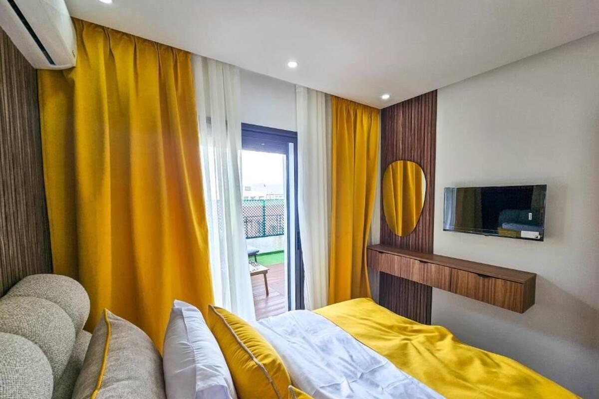 A hotel room with a bed, a sofa, a TV, and a balcony with yellow curtains.