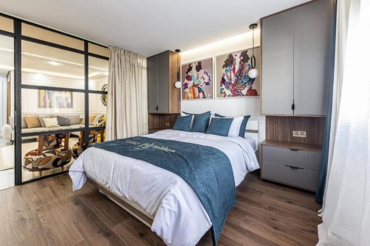 A modern bedroom with a large bed, a sliding glass door leading to a balcony, and a built-in wardrobe.