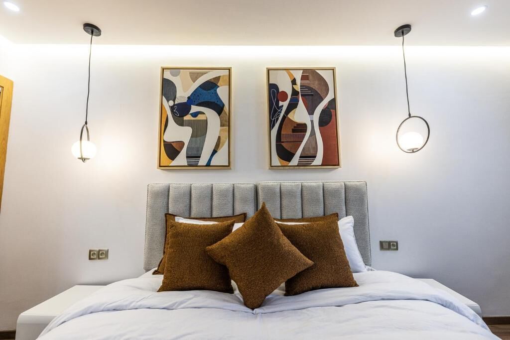 Una camera d'albergo moderna con un letto grande, due quadri astratti appesi al muro e un originale lampadario circolare.
