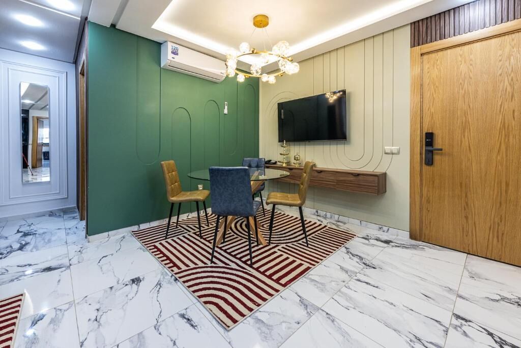 A modern dining area with a marble floor, green accent walls, and a chandelier.