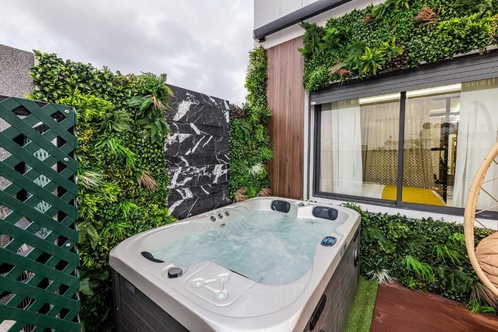 A hot tub in a garden area with a marble wall and lush greenery.