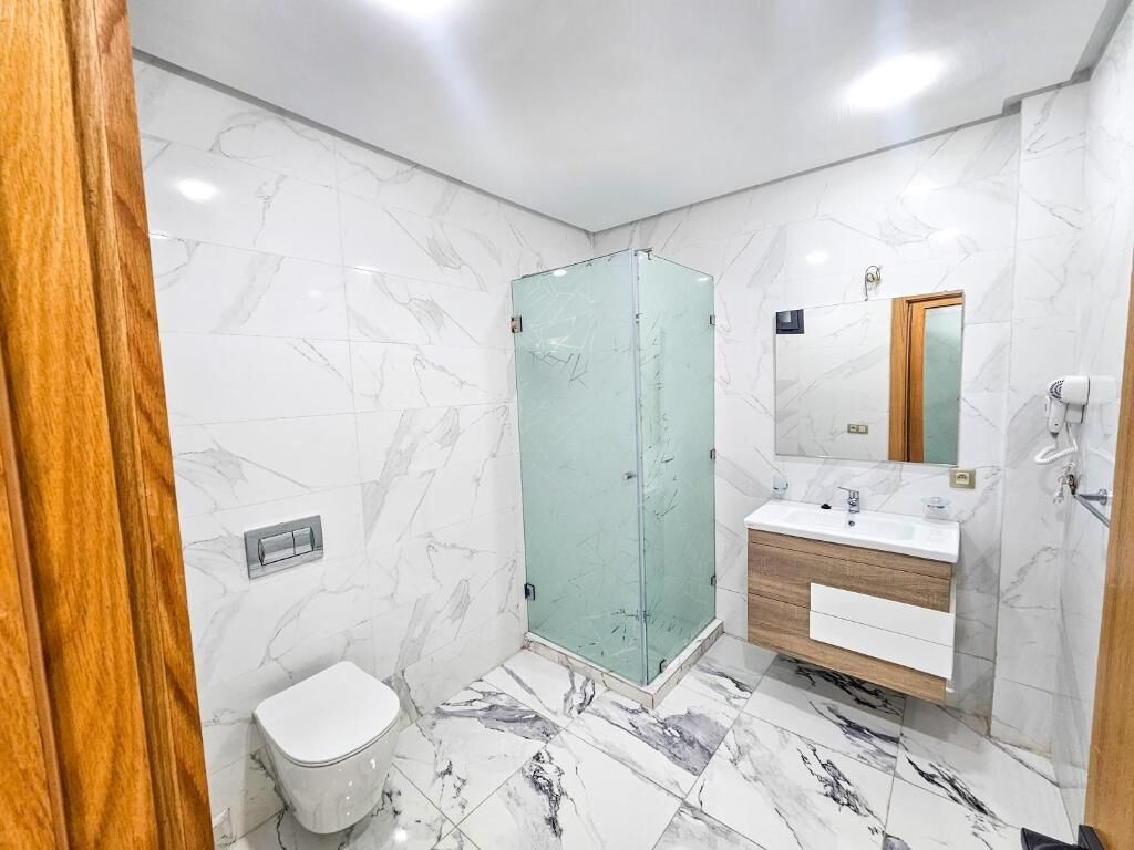 Un baño con piso de mármol, cabina de ducha de vidrio, tocador de madera y retrete.