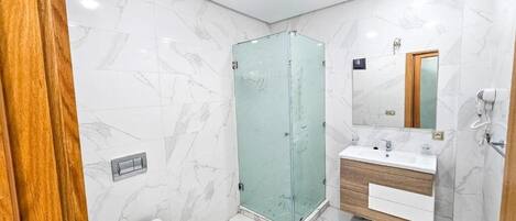Un baño con piso de mármol, cabina de ducha de vidrio, tocador de madera y retrete.