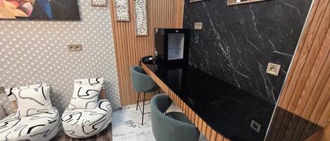A modern room with a curved black countertop, two grey chairs, a TV, and abstract wall art.