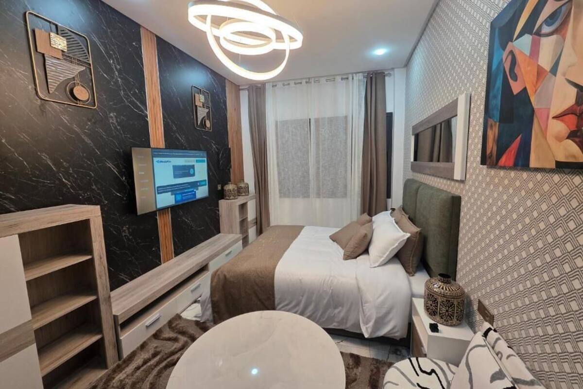 A modern hotel room with a bed, a TV, a desk, and a large painting on the wall.