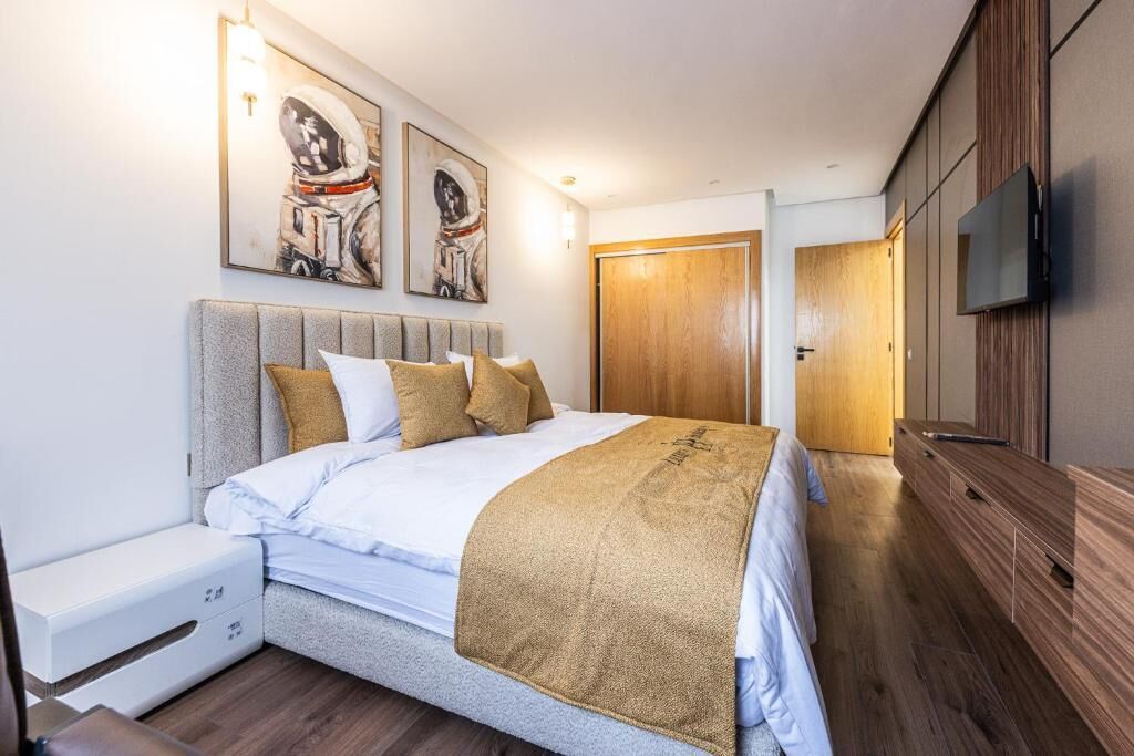 A modern bedroom with a bed, bedside tables, a wooden wardrobe, and a TV mounted on the wall.