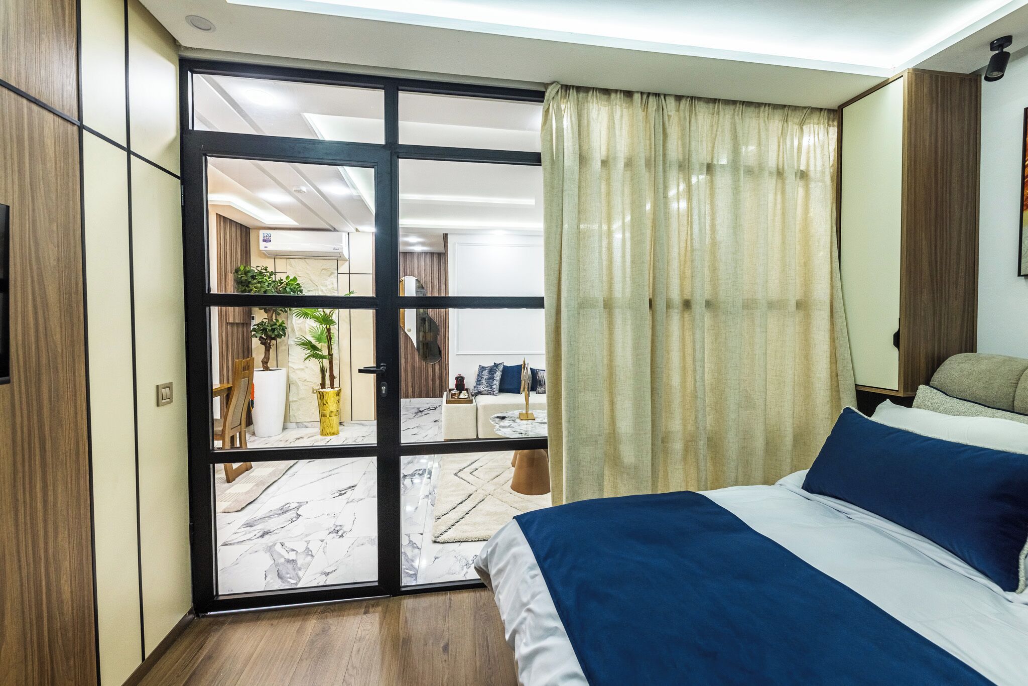 A modern hotel room with a large bed, a sliding glass door leading to a balcony, and a view of the hotel's interior.