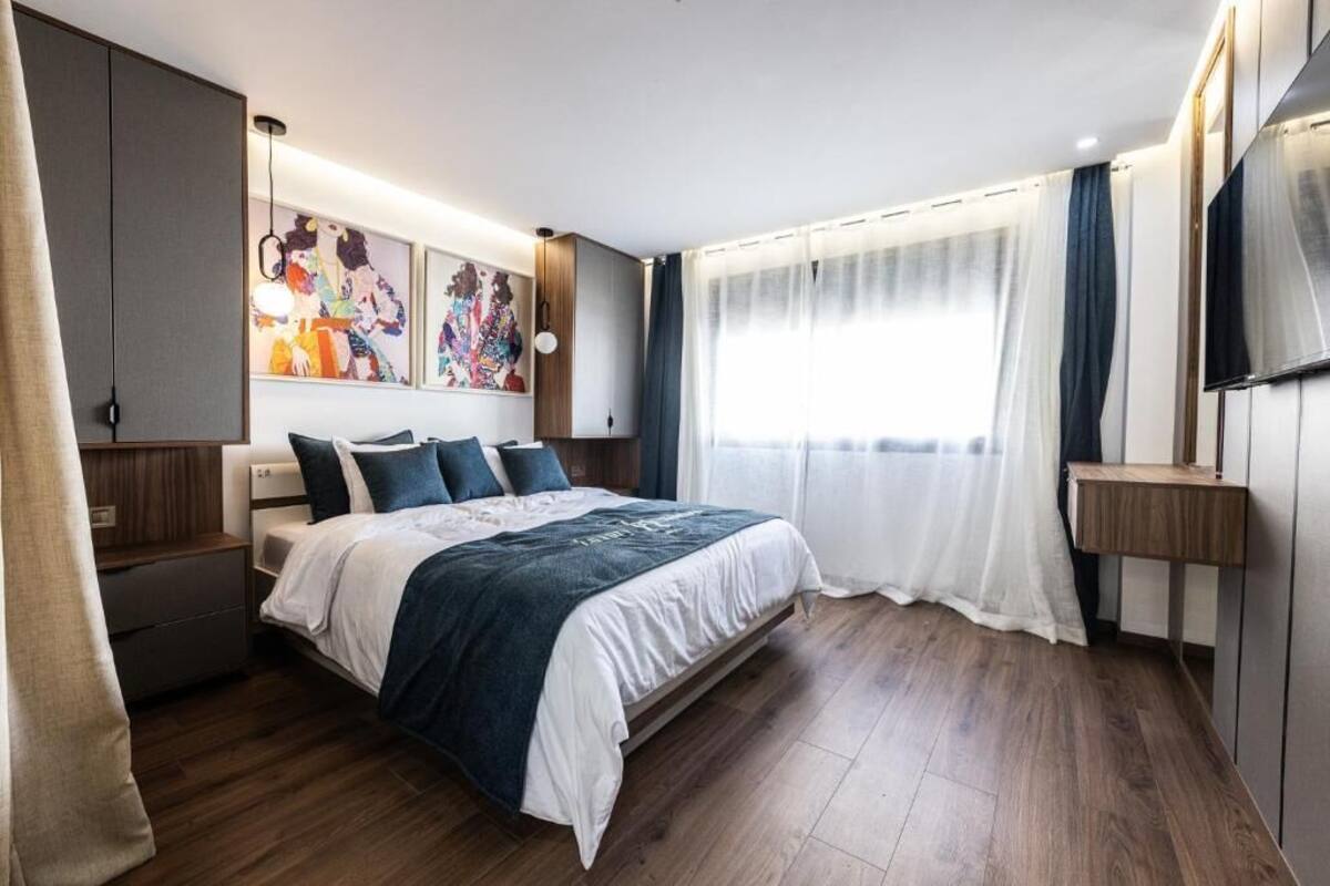 A modern bedroom with a large bed, wooden flooring, and a TV mounted on the wall.