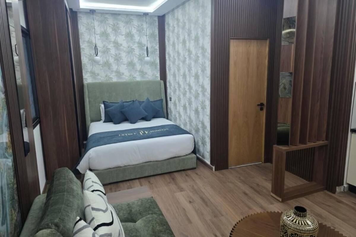A compact bedroom with a bed, a green sofa, a small round table, and a wooden wardrobe.