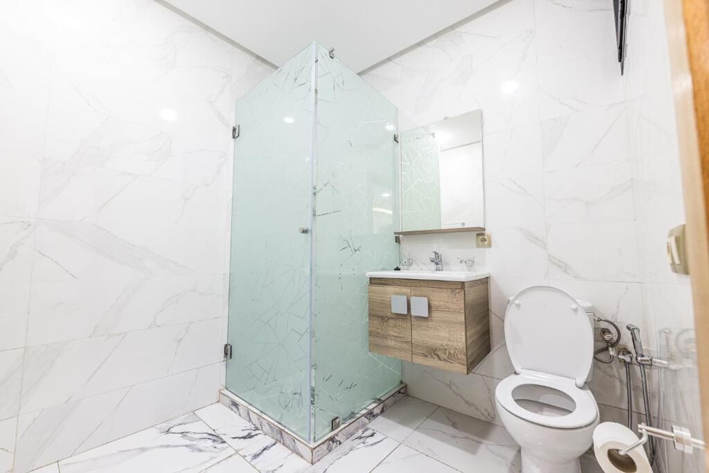 A bathroom with a glass shower enclosure, a wooden vanity, a white toilet, and marble-patterned walls.