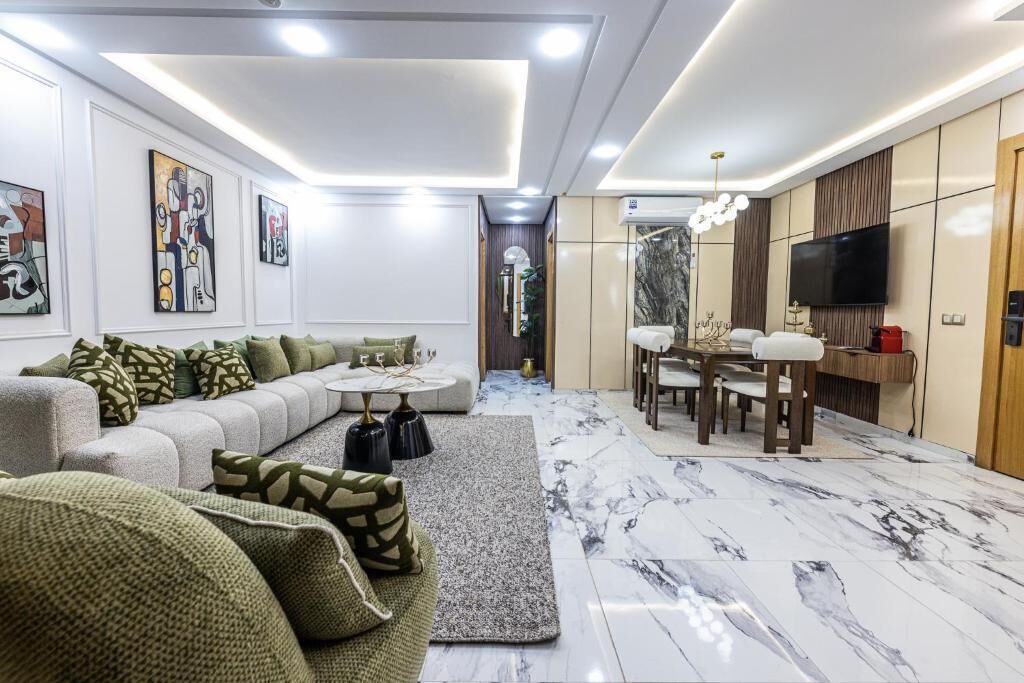 Un salon moderne avec un canapé d’angle, un coin repas comprenant une table et des chaises, et un téléviseur à écran plat fixé au mur.