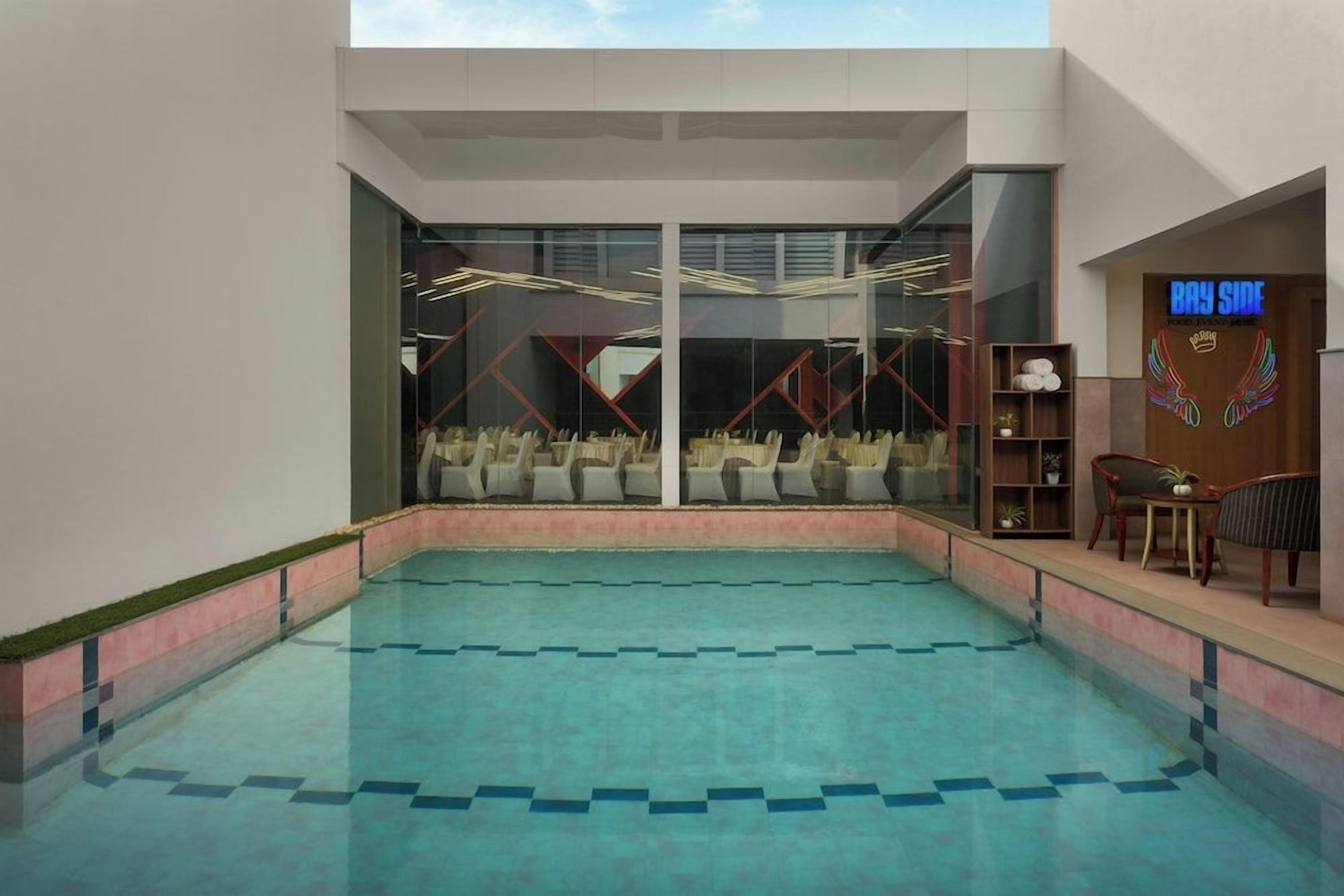 A swimming pool with a view of the sky, a reception area with a sign reading 'Bay Side', and a seating area with chairs and a table.