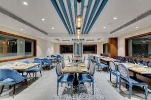 A hotel dining area with multiple tables and chairs, a patterned floor, and a modern ceiling design. - The Fern Residency Hubballi (HUBBALLI)