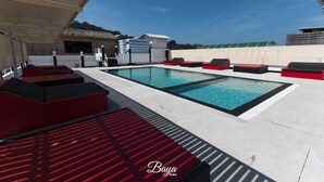 A pool area with red and black lounge chairs, a clear blue pool, and a covered seating area. - Hotel Baya Patong Beach (Patong)