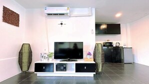 A modern living room with a flat-screen TV, a built-in air conditioner, and a kitchen area in the background. - Hotel Baya Patong Beach (Patong)