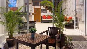 A modern living area with a wooden table and chairs, potted plants, and a sofa with red cushions. - Hotel Baya Patong Beach (Patong)