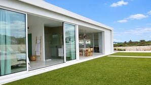 Ein modernes Haus mit großen Schiebeglastüren, die zu einem überdachten Außenbereich mit Tisch und Stühlen führen.