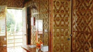 A room with a wooden floor, a ceiling fan, a wooden cabinet with a patterned door, and a small table with a vase of flowers. - Panglao Chocolate Hills Resort (Panglao)