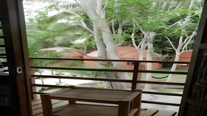 A wooden bench on a balcony with a view of trees and a building in the background. - Panglao Chocolate Hills Resort (Panglao)