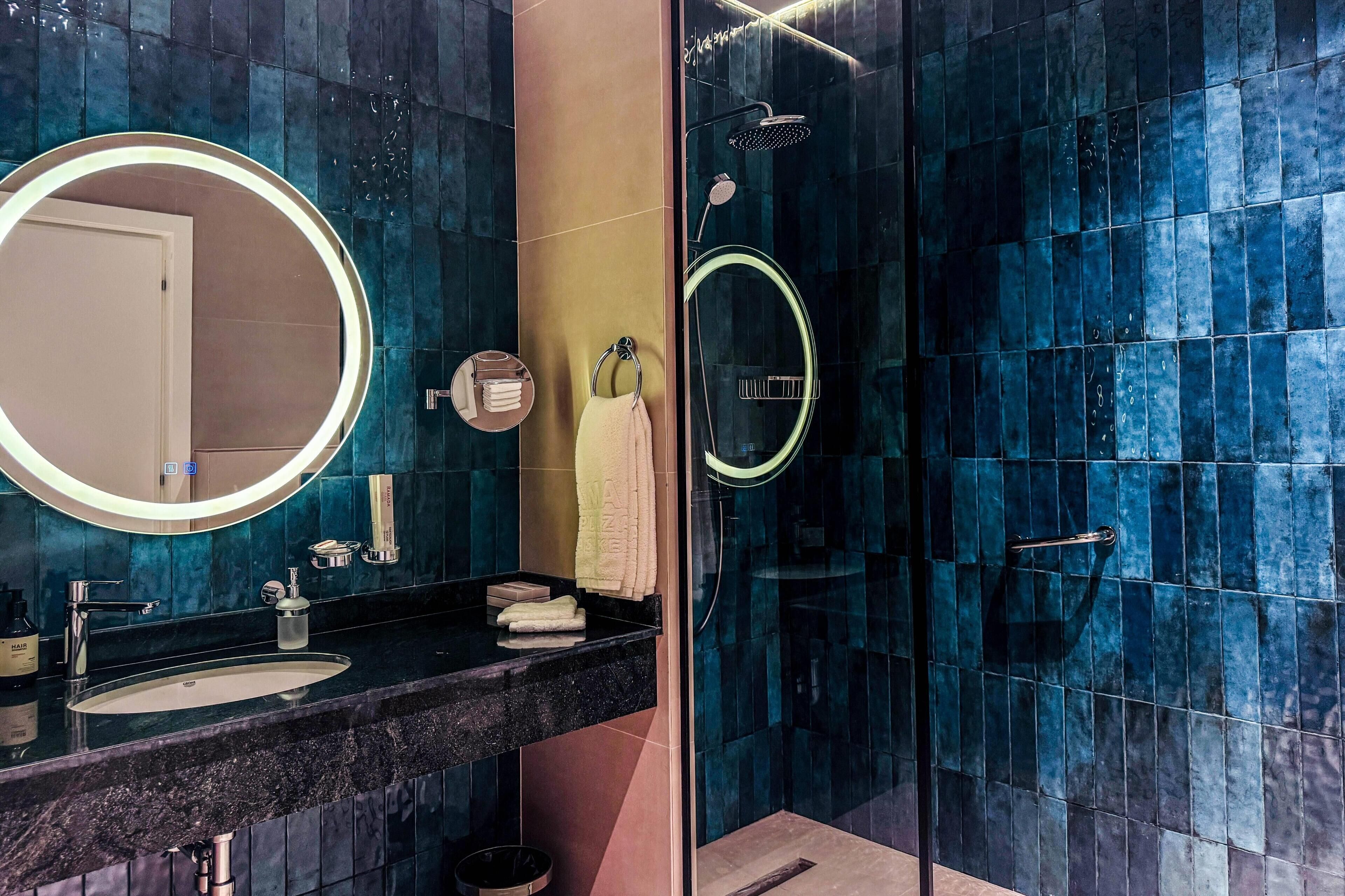 A modern bathroom with a round mirror, a sink, and a glass-enclosed shower area.