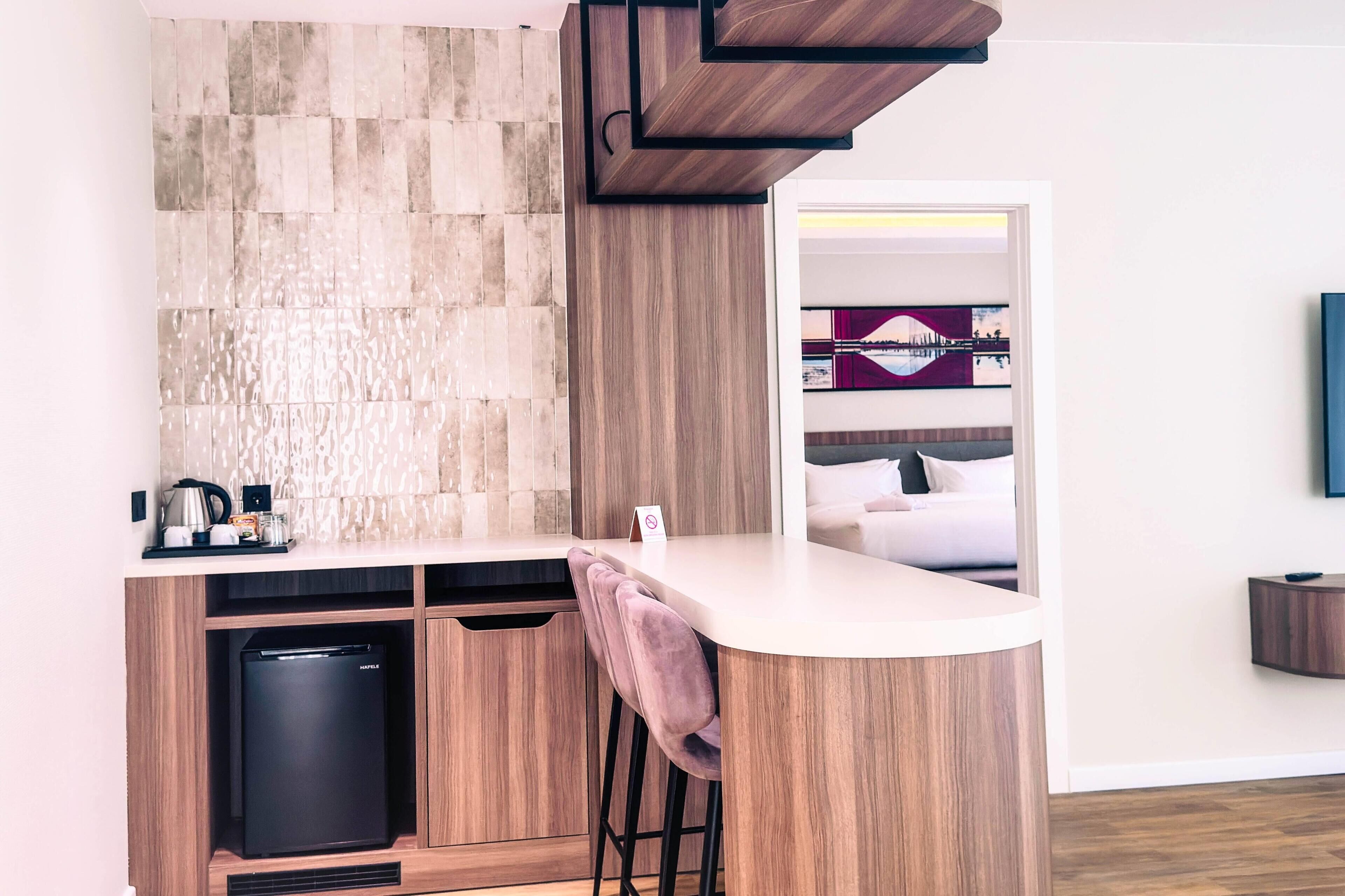 A modern kitchen with a built-in dishwasher, a bar area with stools, and a view of a bedroom with a bed and a TV.