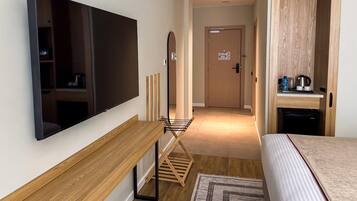 A hotel room with a flat-screen TV, wooden furniture, a small table, a drying rack, a bed, and a kitchenette area.