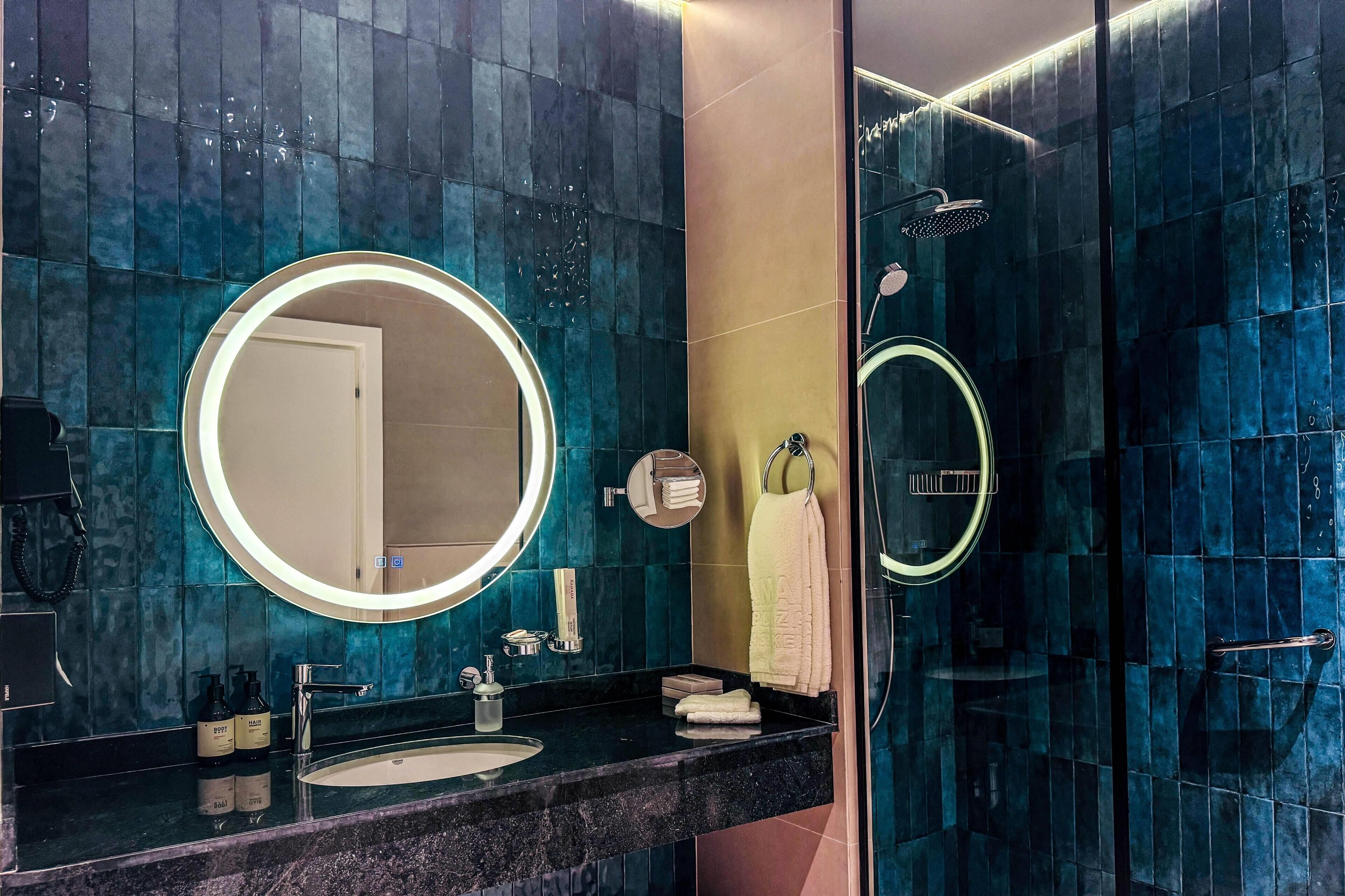 A modern bathroom with a round mirror, a sink, and a shower area.