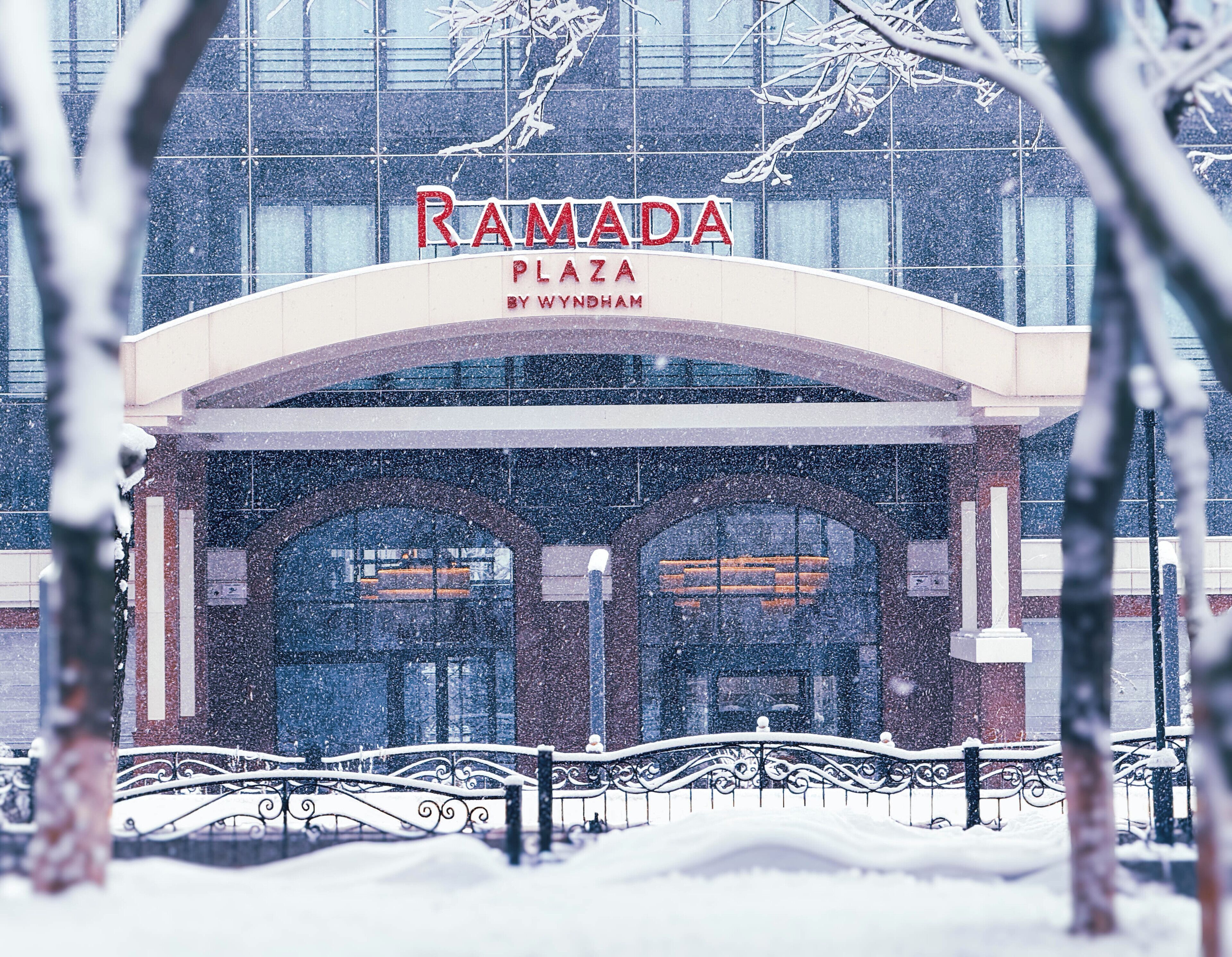 Une entrée enneigée menant à l’hôtel Ramada Plaza by Wyndham, dont l’architecture présente un style moderne.