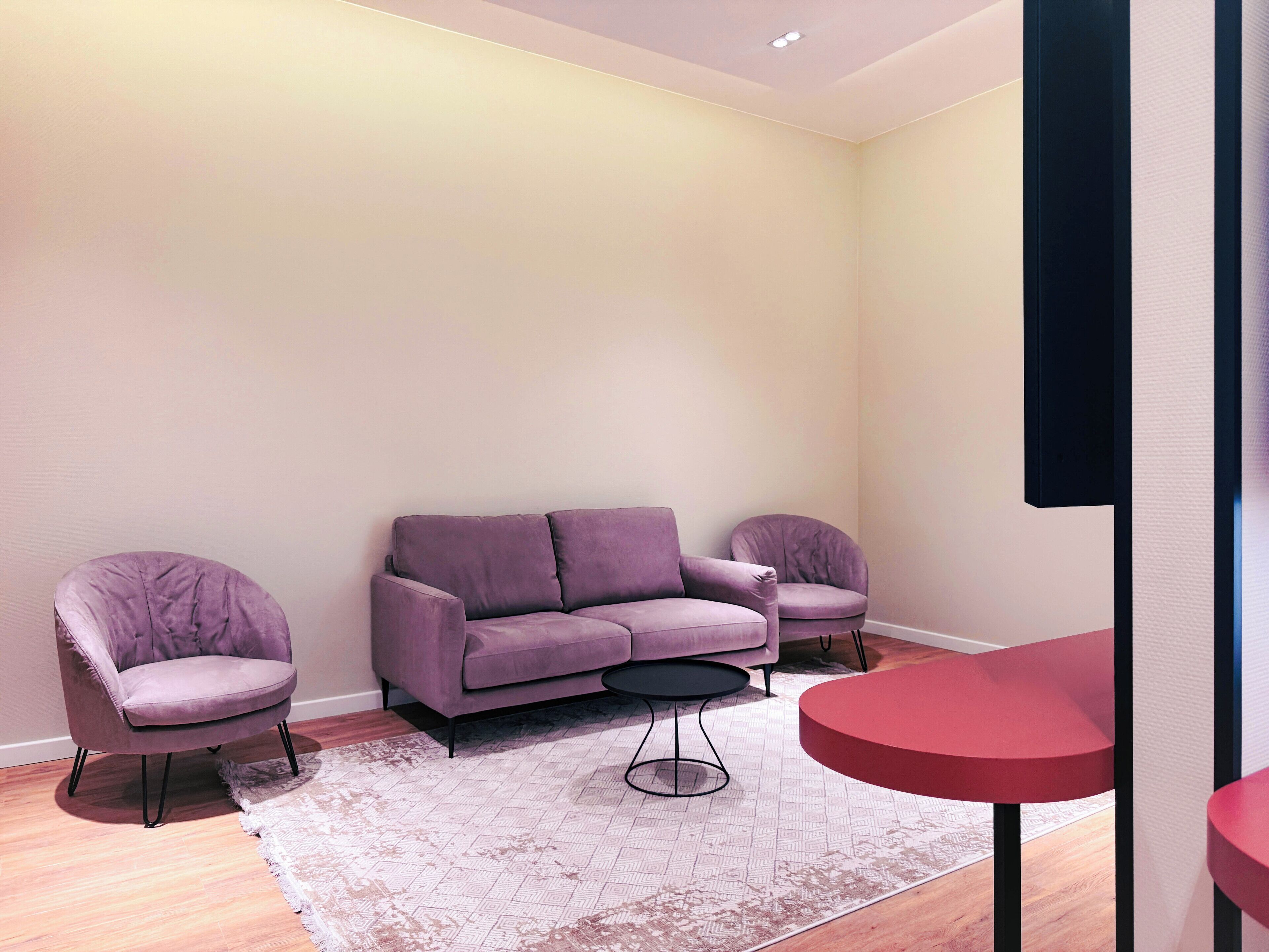Un salon moderne avec un canapé violet, deux fauteuils, une petite table ronde et une table rouge.