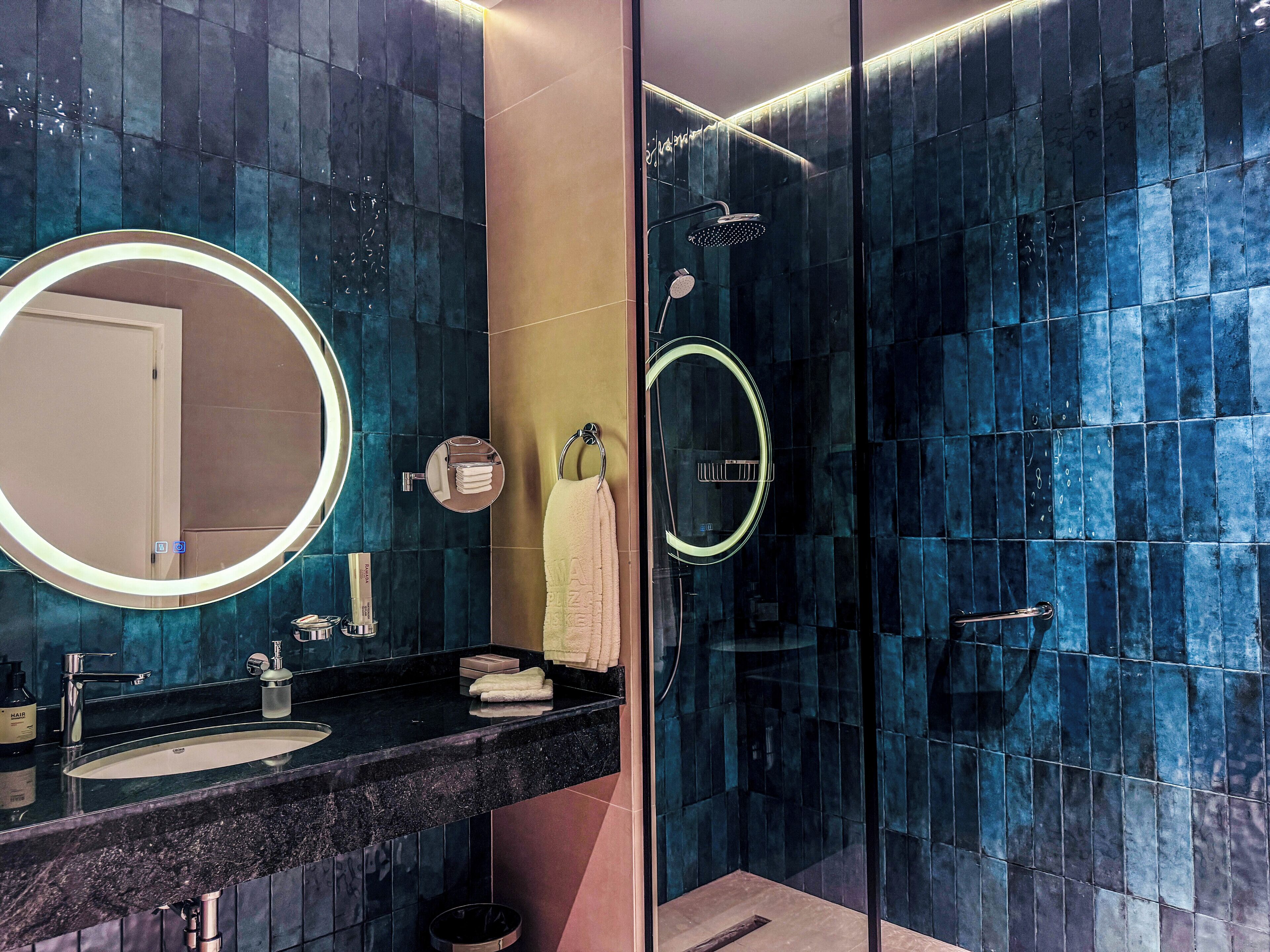 A modern bathroom with a large mirror, a sink, and a glass-enclosed shower.